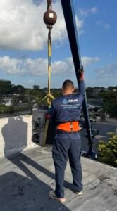 HVAC technician guiding an air conditioning unit onto a rooftop using a crane