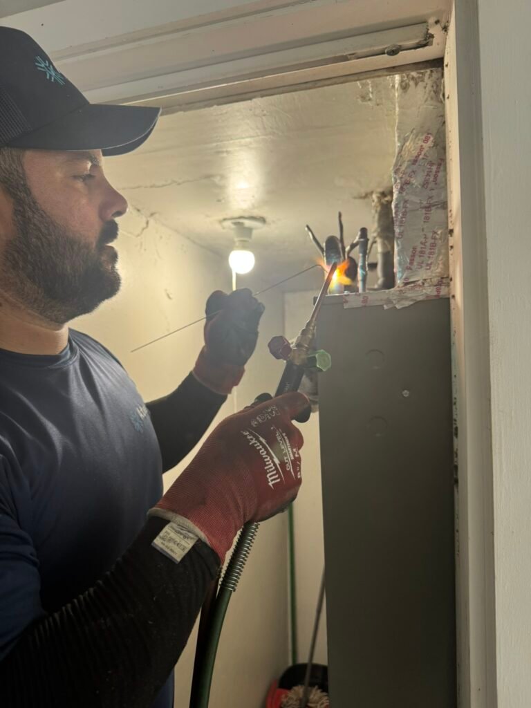 HVAC technician welding copper pipes in an air handler closet unit